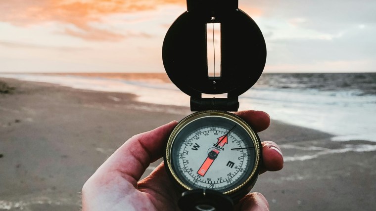 Mano sosteniendo una brújula en la playa, representación de dirección y enfoque.